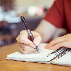 Mano escribiendo en un cuaderno, preparándose para un curso c2 online.