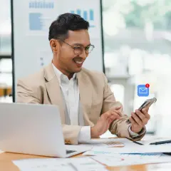 Hombre sonríe revisando su móvil con notificación de email. Busca ejemplos de email formal en inglés para su trabajo.