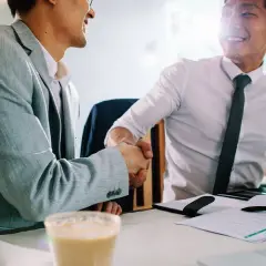 Dos hombres de negocios asiáticos se dan la mano en una cafetería. Uno sonríe, el otro asiente. Gracias por avisar en inglés.