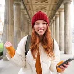 Joven sonríe con un teléfono en la mano, lista para enviar su carta de motivación Erasmus.