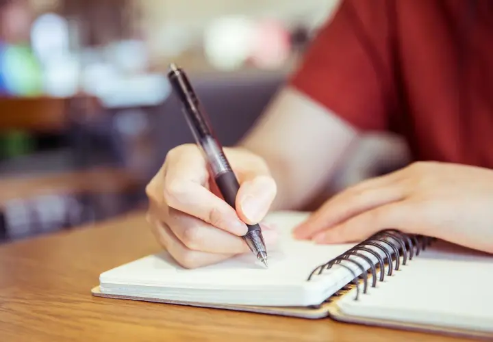 Mano escribiendo en un cuaderno, preparándose para un curso c2 online.