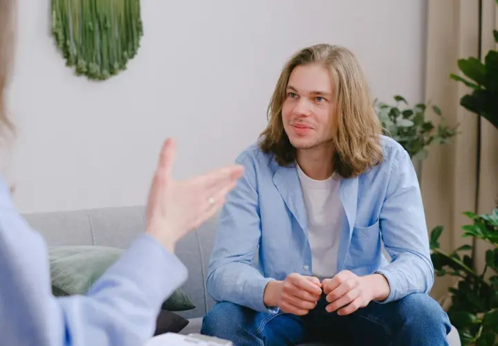 Un joven con cabello largo escucha atentamente en una sesión. Su terapeuta le da una recomendación en inglés.