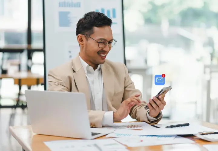 Hombre sonríe revisando su móvil con notificación de email. Busca ejemplos de email formal en inglés para su trabajo.