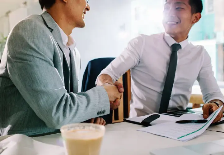 Dos hombres de negocios asiáticos se dan la mano en una cafetería. Uno sonríe, el otro asiente. Gracias por avisar en inglés.