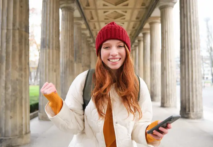 Joven sonríe con un teléfono en la mano, lista para enviar su carta de motivación Erasmus.