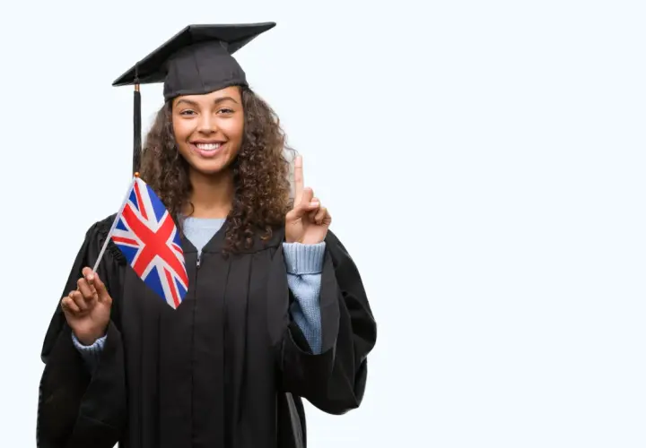 Graduada con toga y birrete, sostiene la bandera del Reino Unido y levanta un dedo, lista para su b1 ingles first.