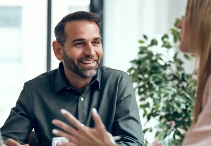 Hombre sonriente con barba, compartiendo ideas y mostrando emociones en inglés durante una conversación.