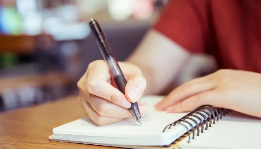 Mano escribiendo en un cuaderno, preparándose para un curso c2 online.