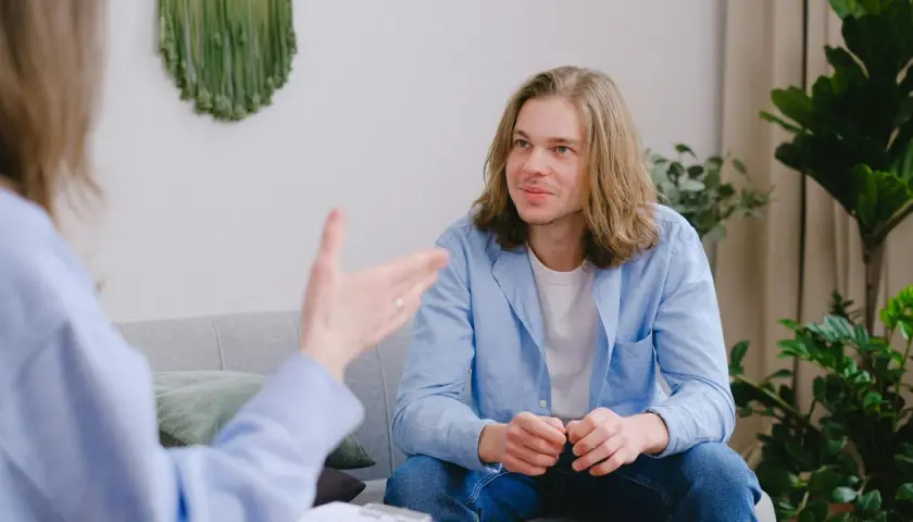 Un joven con cabello largo escucha atentamente en una sesión. Su terapeuta le da una recomendación en inglés.