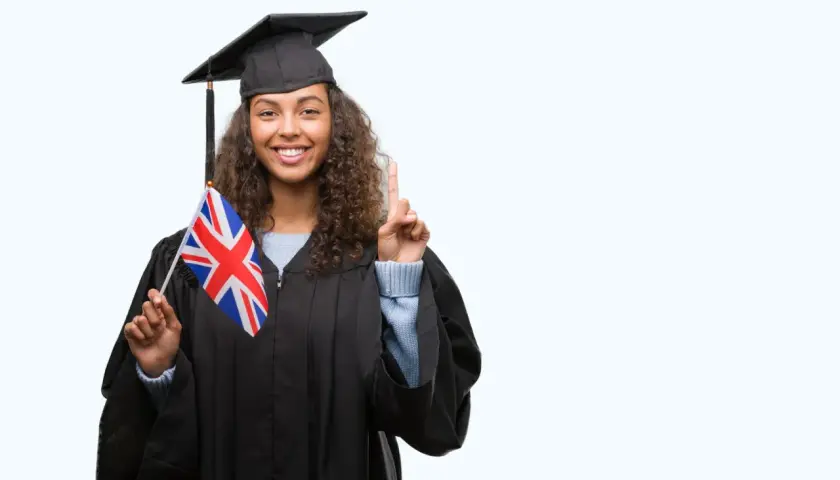 Graduada con toga y birrete, sostiene la bandera del Reino Unido y levanta un dedo, lista para su b1 ingles first.