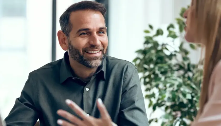 Hombre sonriente con barba, compartiendo ideas y mostrando emociones en inglés durante una conversación.