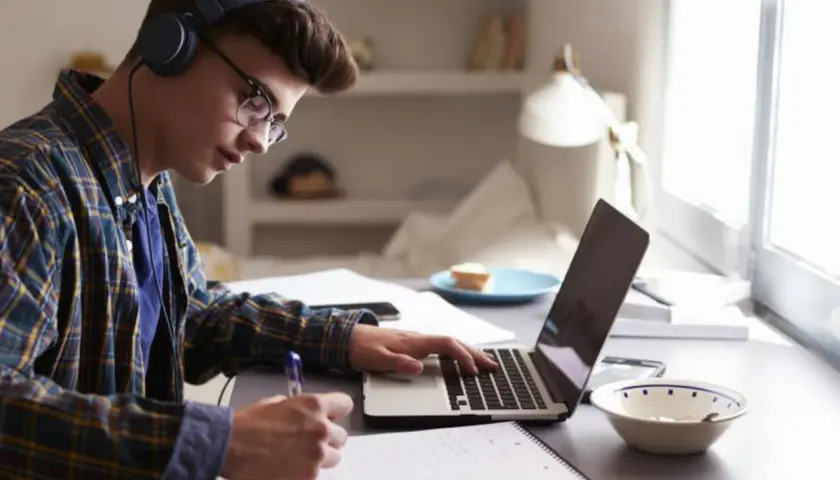 Joven concentrado estudiando con auriculares y portátil, preparándose para como sacarse el first por libre.