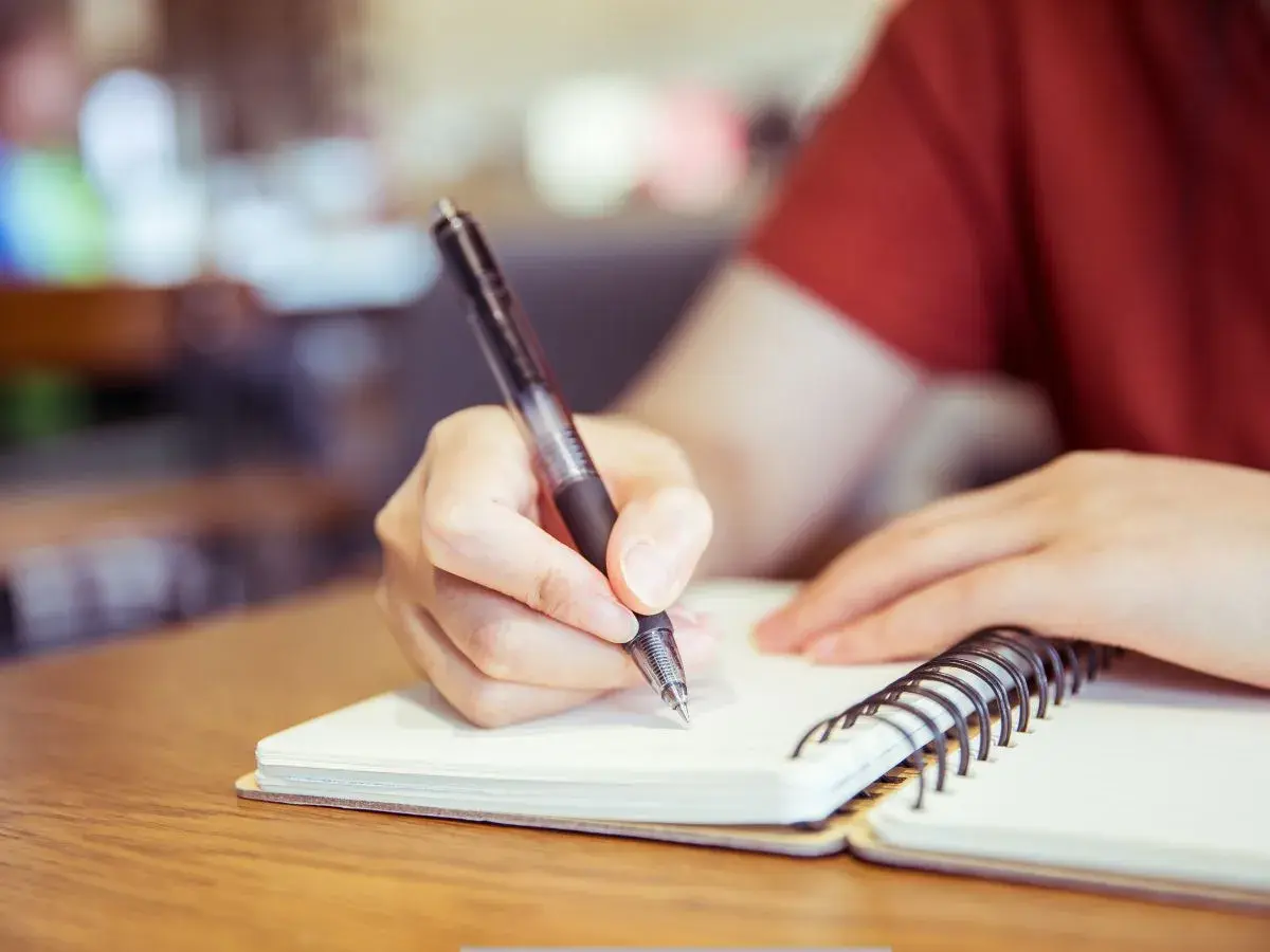 Mano escribiendo en un cuaderno, preparándose para un curso c2 online.