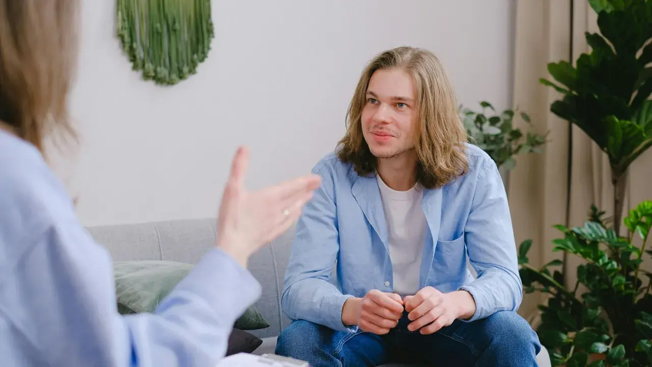 Un joven con cabello largo escucha atentamente en una sesión. Su terapeuta le da una recomendación en inglés.