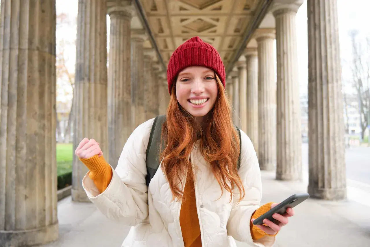 Joven sonríe con un teléfono en la mano, lista para enviar su carta de motivación Erasmus.