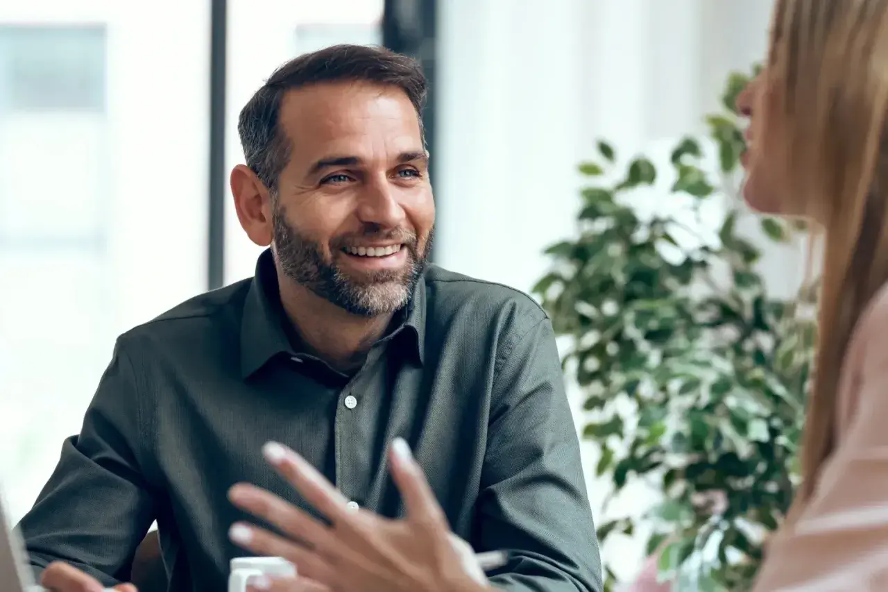 Hombre sonriente con barba, compartiendo ideas y mostrando emociones en inglés durante una conversación.