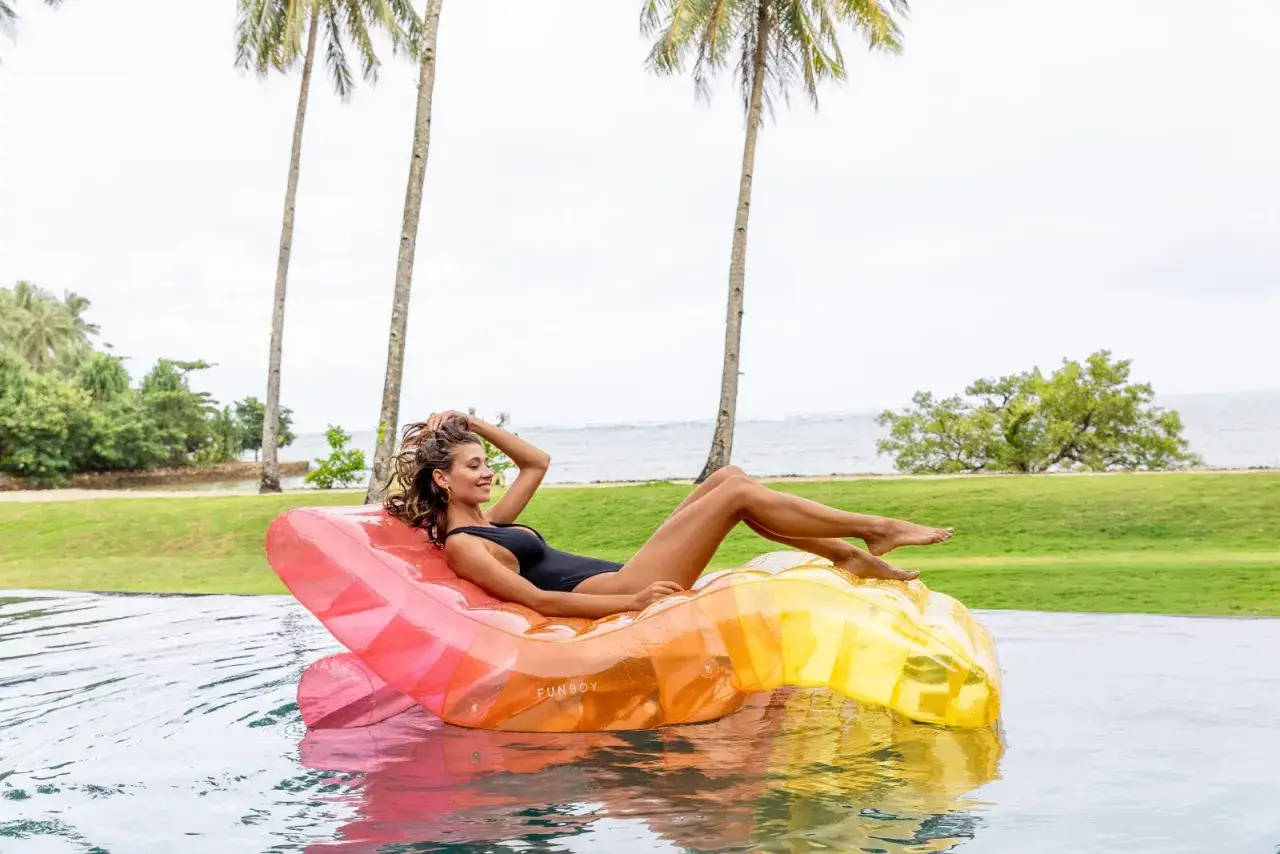 Mujer relajada en un flotador inflable de colores vibrantes, rodeada de palmeras y el mar. ¡Perfecto para el vocabulario de verano!